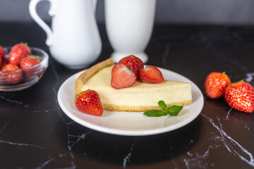 Classic sliced homemade New York cheesecake with fresh strawberries served on a black marble countertop. Homemade dessert.