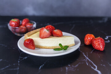 Classic sliced homemade New York cheesecake with fresh strawberries served on a black marble countertop. Homemade dessert.