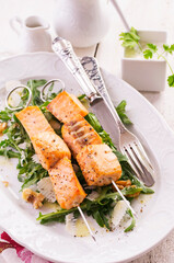 Traditional grilled salmon skewer with rucola salad, parmesan cheese and walnuts served as close-up on a classic design plate
