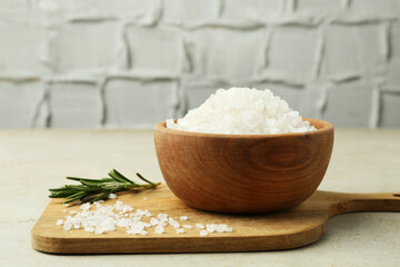 Sea salt in bowl and rosemary on grey table, closeup