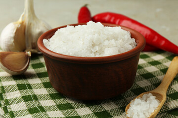 Sea salt in bowl, garlic and chili peppers on table, closeup