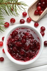 Tasty cranberry sauce in bowl, berries and fir tree branches on white wooden table, top view