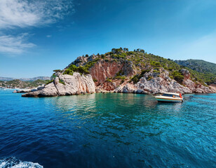 Obraz premium A luxury yacht anchored near a dramatic rocky coastline with crystal-clear turquoise waters and lush green vegetation atop the cliffs on a bright sunny day in Aegean Türkiye