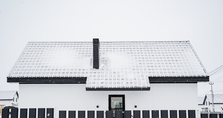 A charming white house featuring a black chimney perched on its roof is beautifully blanketed in a layer of fresh snow, creating a picturesque winter scene that captivates the eye