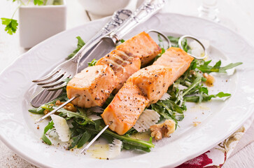 Traditional grilled salmon skewer with rucola salad, parmesan cheese and walnuts served as close-up on a classic design plate