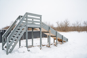A metal staircase, partly covered in soft snow, stands amidst a picturesque winter landscape with tall trees, evoking a serene atmosphere that invites appreciation of nature