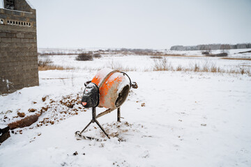 A heavyduty concrete mixer sits motionless in thick snow outside a sturdy building, surrounded by a...