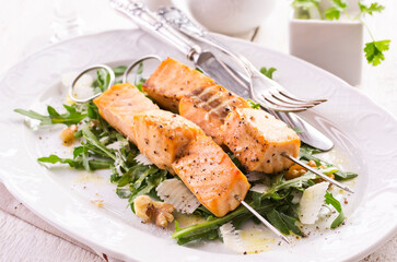 Traditional grilled salmon skewer with rucola salad, parmesan cheese and walnuts served as close-up on a classic design plate