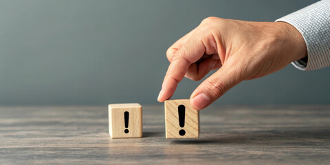A hand in a business shirt places a wooden block with an exclamation mark next to another similar block on a wooden surface. It suggests emphasizing caution or highlighting important information. AI 