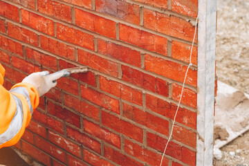 Bricklayer builder applying mortar to brick wall at construction site during daylight