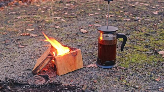 Male Hiker Tourist Pouring Boiling Hot Water into Ground Coffee Brewing French Press Jug at Improvised Camp Site with Buddy Burner Stove