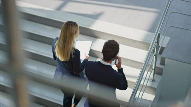 Business partners discussing documents walking up stairs modern office building