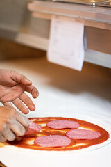 Hands preparing a pizza putting salami on pizza