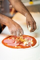 Hands preparing a pizza putting salami on pizza