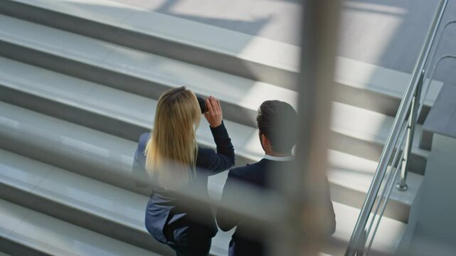 Two professionals walking up stairs modern office building. Smiling colleagues
