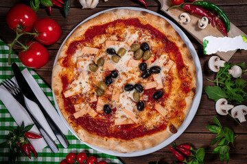 Delicious hot pizza with salmon, olives, tomatoes and spices on wooden table