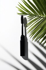 Black tube of mascara with a long wavy brush on a white background and a green palm tree
