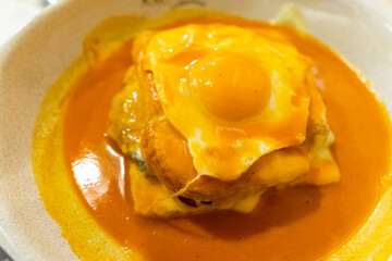 Traditional Portuguese Francesinha sandwich served on a restaurant table, topped with melted cheese and savory sauce, capturing authentic Porto cuisine and dining culture.
