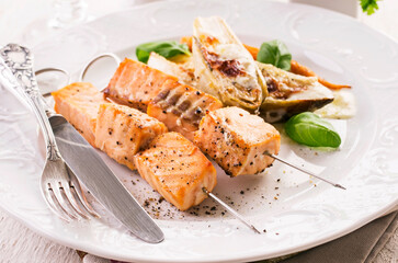 Traditional grilled salmon skewer with chicory salad, carrots and bechamel sauce served as close-up on a classic design plate