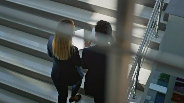 Business couple climbing stairs discussing documents. Successful businessman