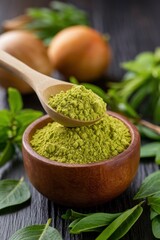 Green powder in a wooden bowl with fresh leaves and onions