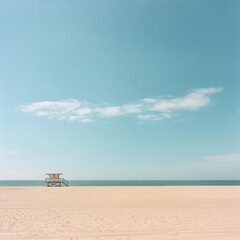 Obraz premium Solitary lifeguard stand on a serene beach under a pale blue sky.