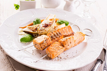 Traditional grilled salmon skewer with chicory salad, carrots and bechamel sauce served as close-up on a classic design plate