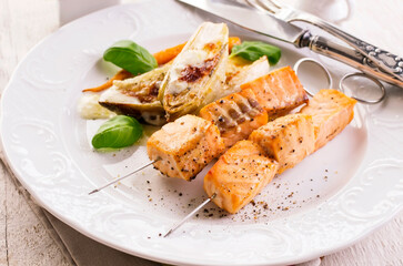 Traditional grilled salmon skewer with chicory salad, carrots and bechamel sauce served as close-up on a classic design plate