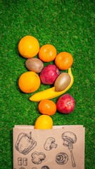 Banana, red apple and different fruits with craft paper bag laying on grass, flat lay. Space for text. Zero waste concept.