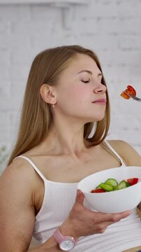 Young woman eating salad. Beautiful girl sniffing and eating organic vegetables on the kitchen background. Natural food concept. Vertical video