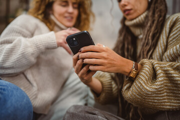 Fototapeta premium two adult female friends sit on sofa and enjoy while use cellphone