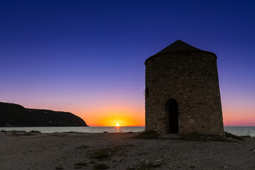 Kolorowy zachód słońca  z widokiem na stary wiatrak nad morzem na piaszczystej plaży, grecka wyspa Lefkada, krajobraz © anettastar