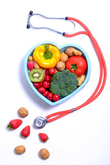 Heart shaped dish with vegetables and stethoscope isolated on white background