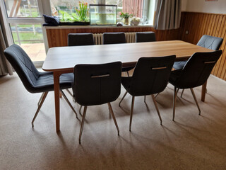 Fototapeta premium home dining table made of beech wood. around there are 8 chairs with upholstery and geometric stitching. an empty table top without a tablecloth suitable for advertising purposes.