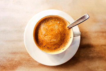 Top view of cup of foamy coffee on wooden table, central composition, image in brown tones