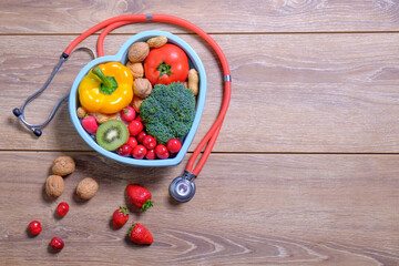Heart shaped dish with vegetables and stethoscope isolated on wooden background