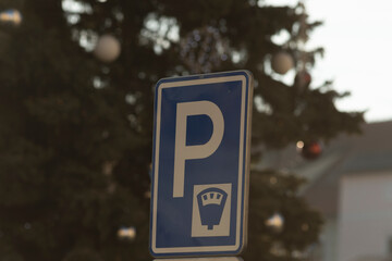 A parking sign can be seen positioned close to a beautifully decorated Christmas tree situated in...