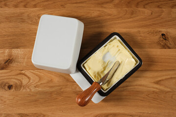 A butter dish lying on a wooden table, together with a grease knife