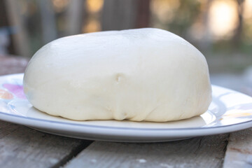 A large, round piece of dough on a plate, a white and very soft-looking piece of cream cheese with a rounded shape and smooth texture