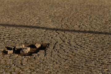 The cracked pavement visibly reveals scattered stones strewn across a disturbed area located on the ground underneath