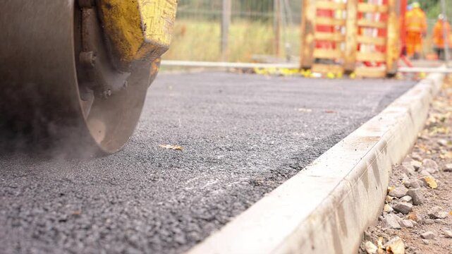 Construction workers complete a new asphalt pathway in a community area during autumn