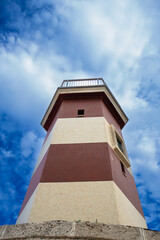 Red and white striped lighthouse landmark in beautiful port in Monopoli, Italy under a cloudy stormy sky