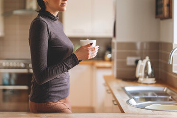 Woman enjoying a warm beverage while standing by the kitchen sink during morning hours