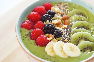 A green smoothie bowl topped with fresh kiwi slices, raspberries, blackberries, banana slices, almonds, chia seeds, and granola, perfect for a healthy vegan breakfast.