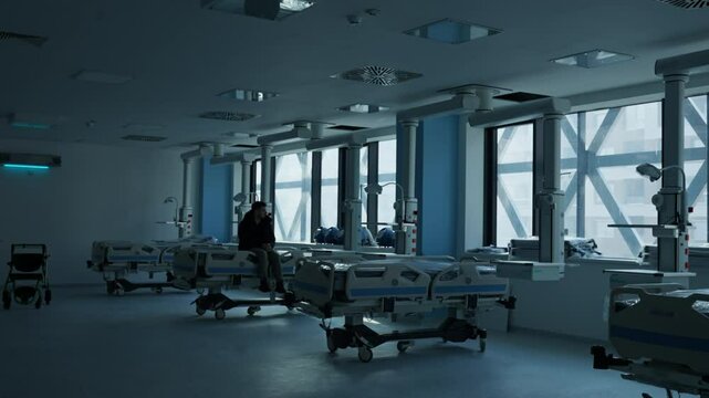 Man sits quietly on a hospital bed in a dimly lit, empty medical facility, evoking a sense of reflection and loneliness. Concept of isolation, waiting, and uncertain emotions in a healthcare setting.