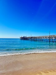 A wooden pier extending into the Pacific Ocean as viewed from the beach