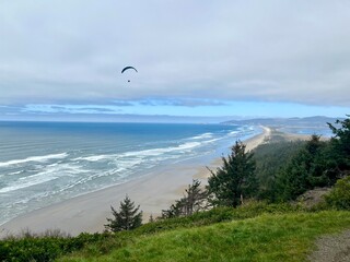 Paraglider flying over the beach and the Pacific Ocean along the coast in Oregon, USA