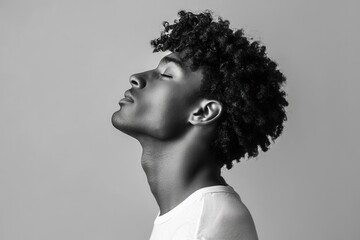 Attractive curly haired Black man in a t shirt against a gray backdrop side profile