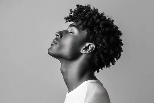 Attractive curly haired Black man in a t shirt against a gray backdrop side profile