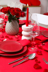 Festive table setting decorated for Valentine's Day with red roses and burning candles at home